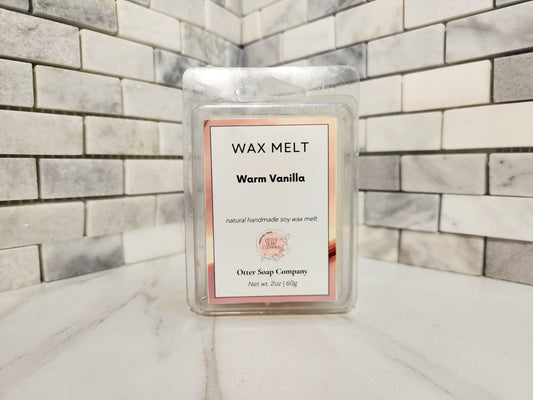 A single wax melt package labeled 'Warm Vanilla' by Otter Soap Company, standing upright on a marble-like surface against a gray and white tiled wall.